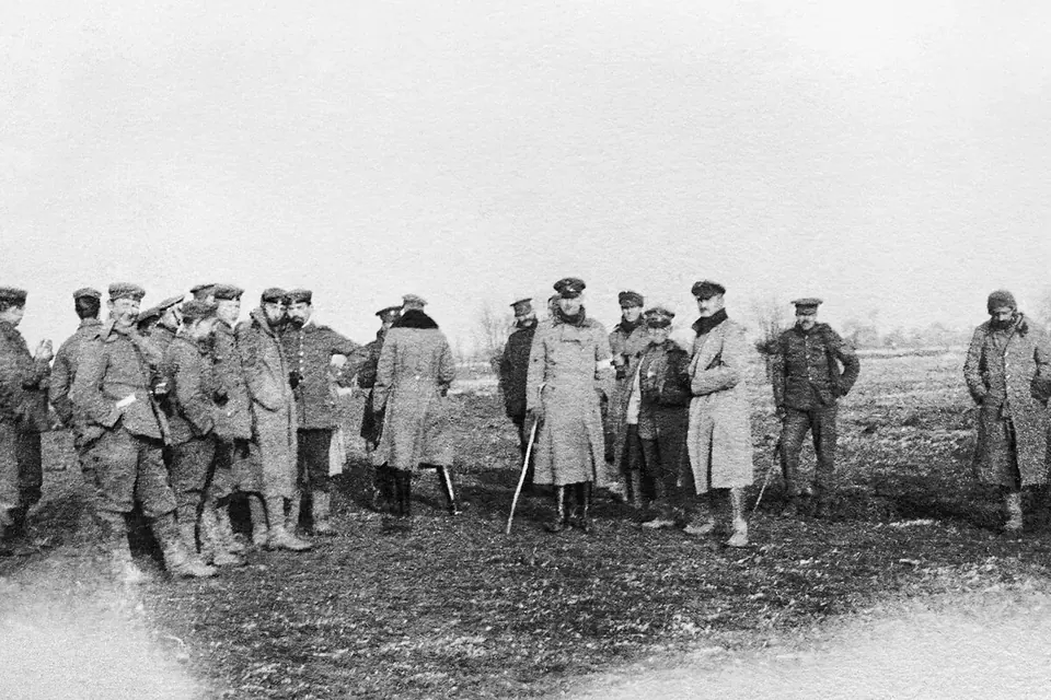 Black and white photograph of British and German soldiers in greatcoats standing together on a muddy field