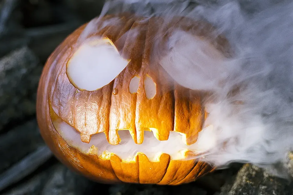 A carved pumpkin lantern glowing orange, with smoke curling out of its eyes and mouth