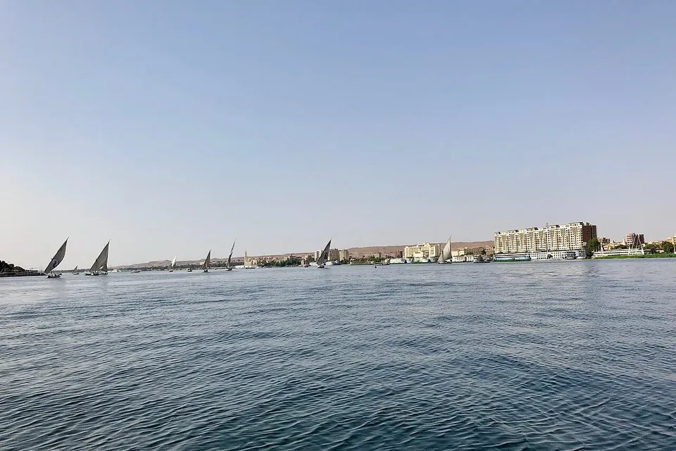 The wide calm Nile under a pale sky, with white-sailed feluccas and buildings on the far bank